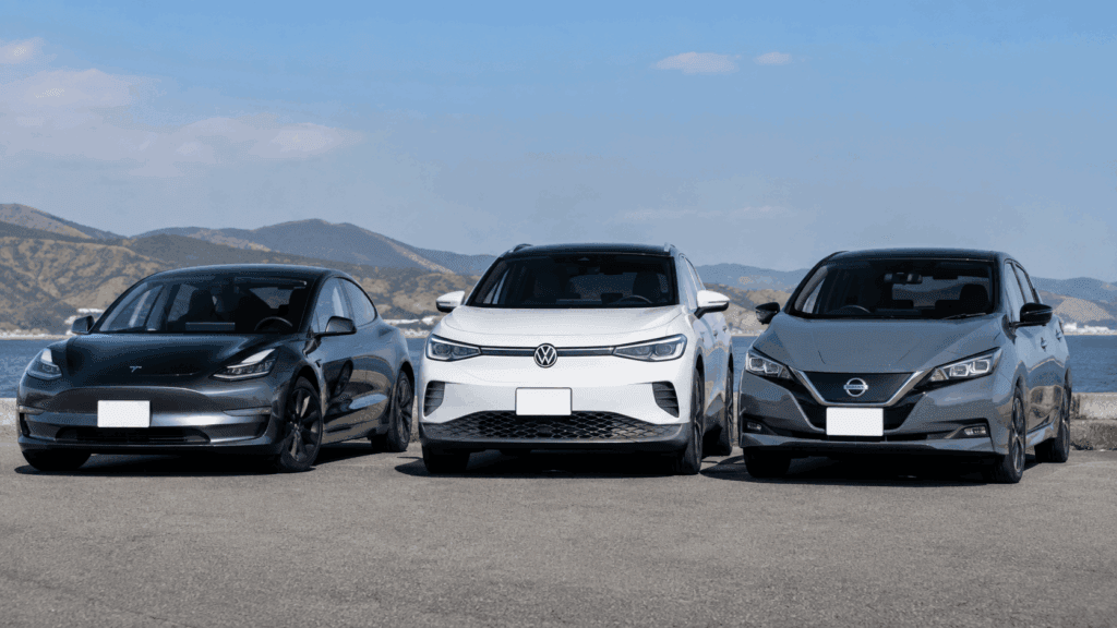 海沿いに並ぶテスラ モデル3、フォルクスワーゲン ID.4、日産リーフのフロント外観写真(国内外EVのバッテリーとリセール比較イメージ)